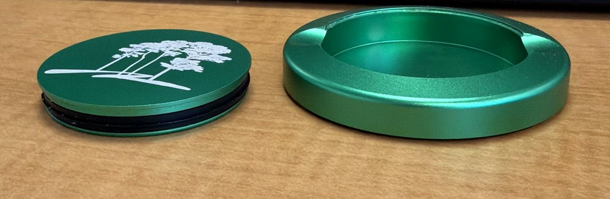 An engraved lid beside the open body of a green Crest & Co. tin.