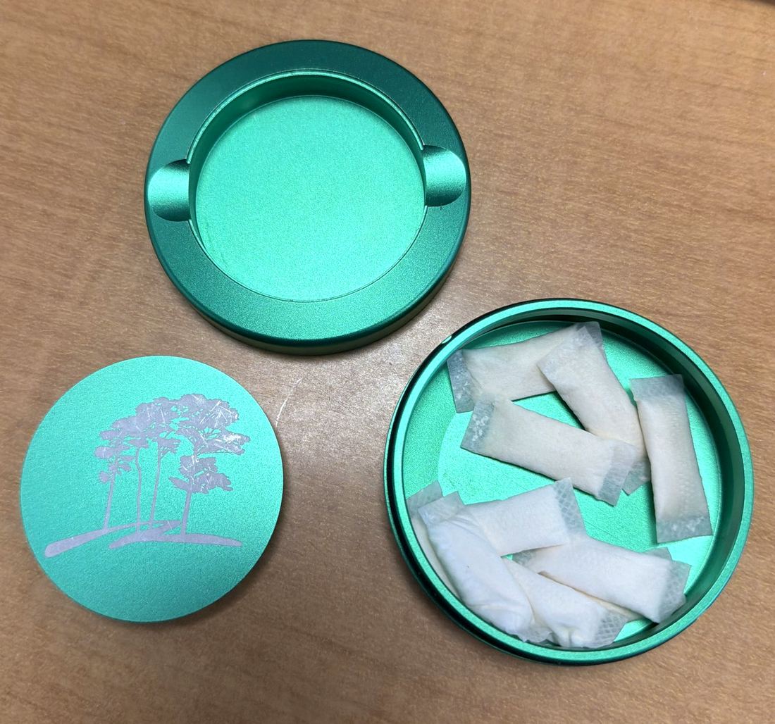 All three pieces of a green Crest & Co. tin laid out: the used tray, the engraved lid, and the base packed with fresh pouches.